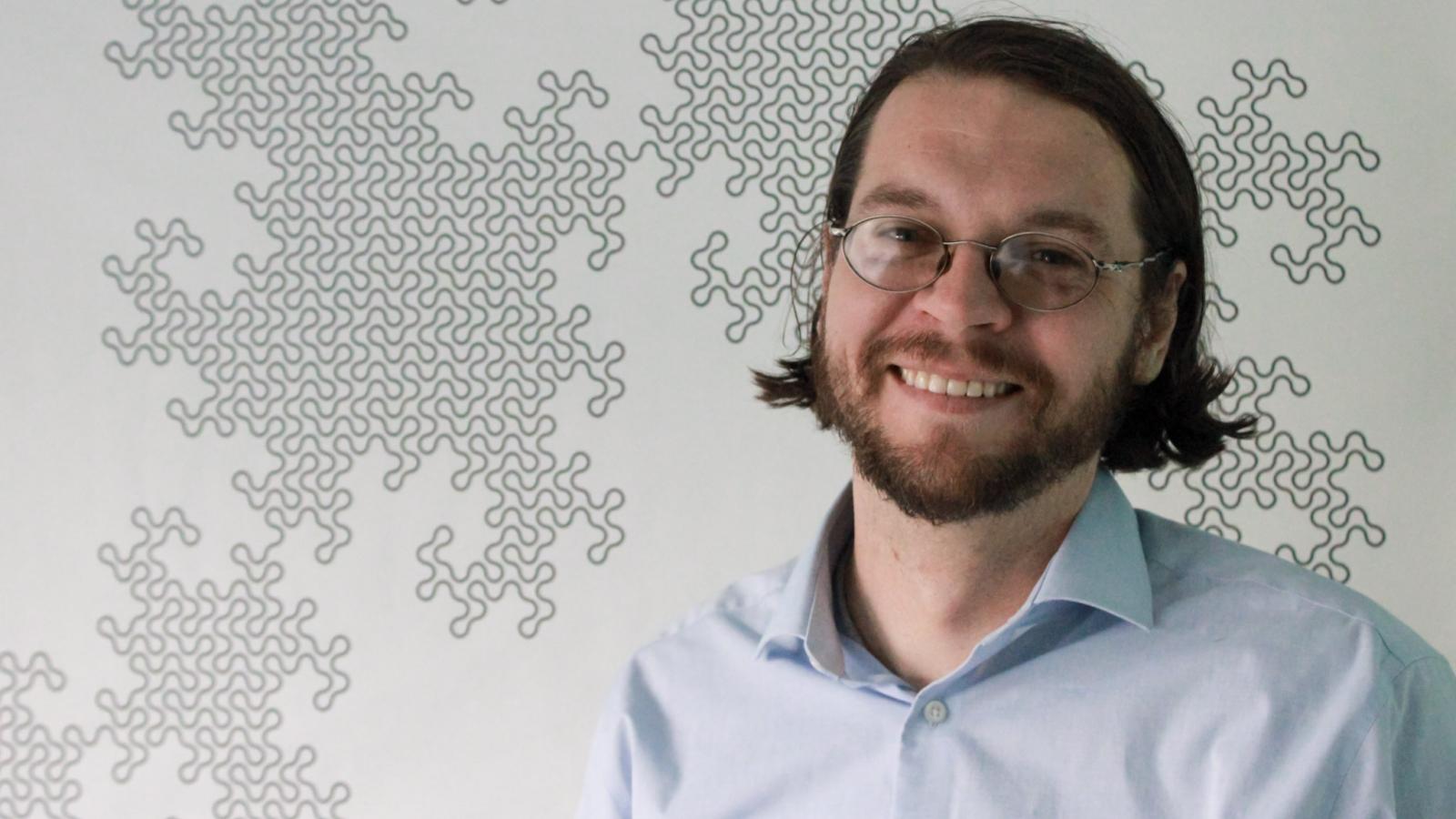Chris Orban standing in front of a fractal pattern